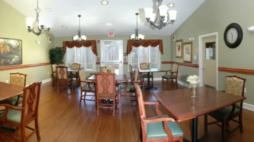 A panoramic shot of a dining room with multiple tables, chairs, chandeliers, and a clock on the wall